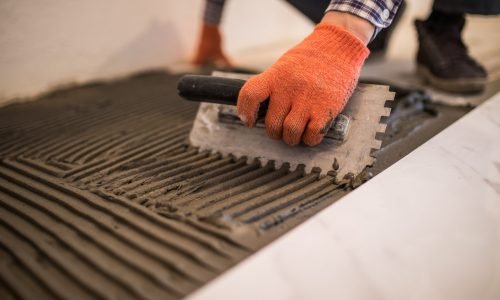 Troweling mortar onto a concrete floor in preparation for laying white floor tile.